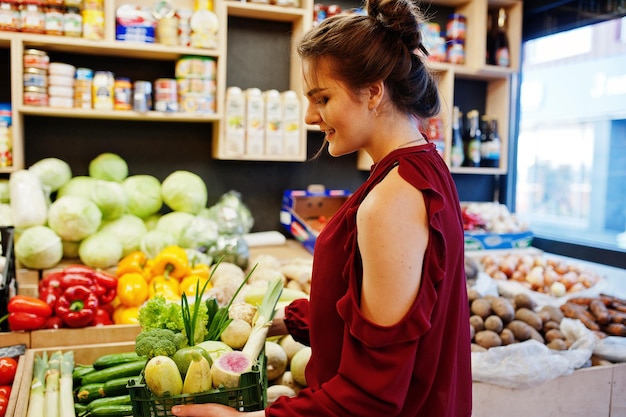 Ragazza in rosso che tiene diverse verdure sul negozio di frutta