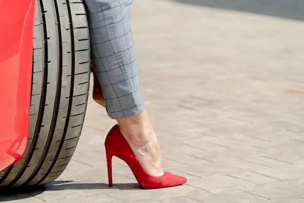 Ragazza in scarpe rosse e un'auto rossa in una giornata di sole estivo.