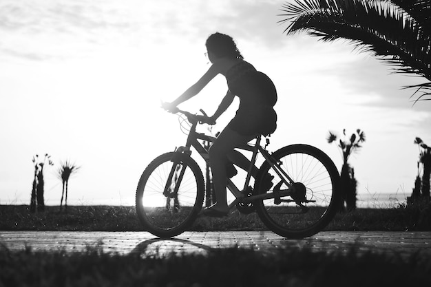 Ragazza in sella a una bicicletta, silhouette al tramonto, foto in bianco e nero