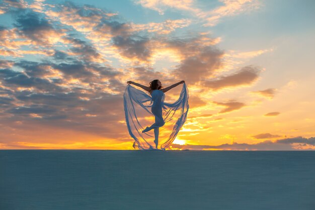 ragazza in un abito bianco vola balla e pone nel deserto di sabbia al tramonto