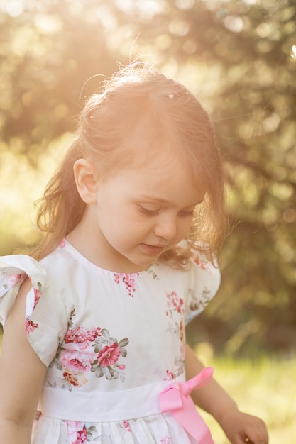 Ragazza in un bel vestito che cammina nel parco o in giardino in primavera. Il bambino gode della natura.