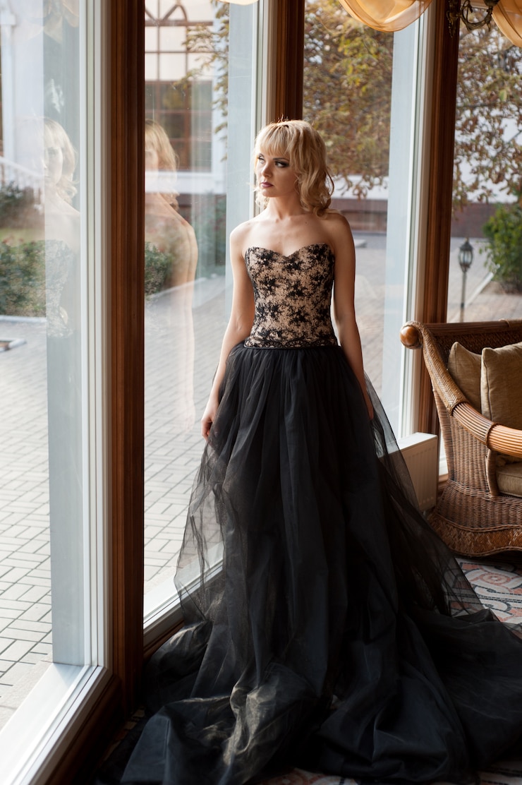 Foto ragazza in un bellissimo abito nero si trova vicino alla finestra e guarda fuori dalla finestra