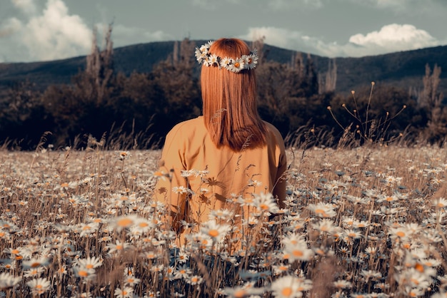Ragazza in un campo di camomilla in fiore vista dal retro