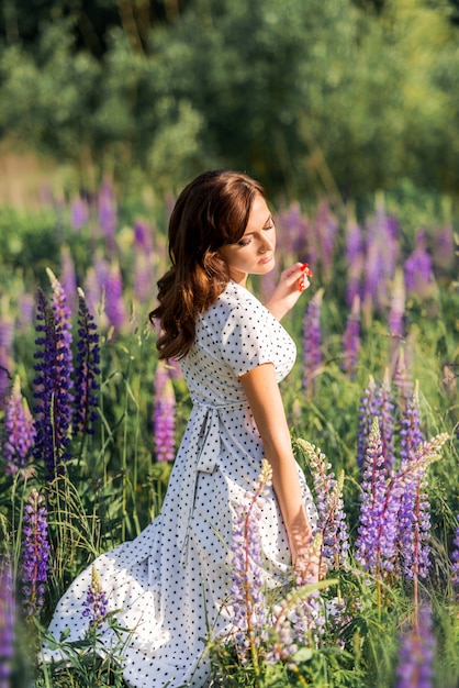 Ragazza in un campo di fiori con lupini. Foto estiva in natura