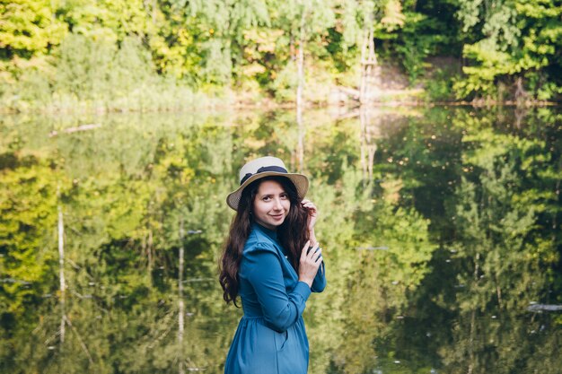 Ragazza in un cappello che riposa sul lago di autunno sul ponte