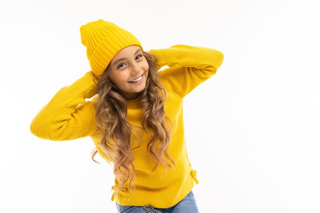 ragazza in un cappello giallo e felpa ha portato le mani dietro la testa su bianco.