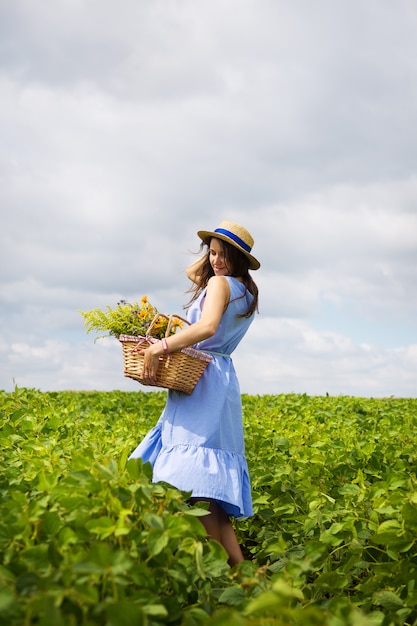 Ragazza in un cappello si trova su un campo verde con un cesto di fiori