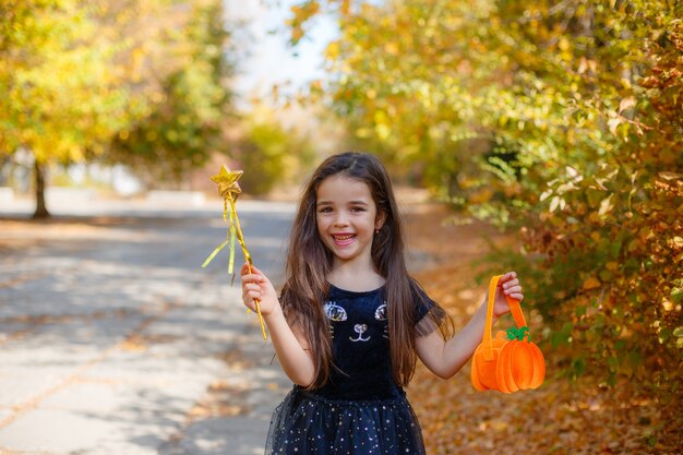 Ragazza in un costume da strega con una bacchetta magica per Halloween nel parco d'autunno