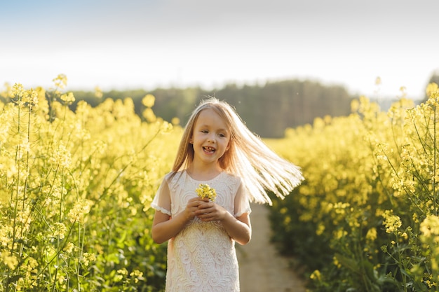 ragazza in un lungo abito bianco in un campo di colza in estate