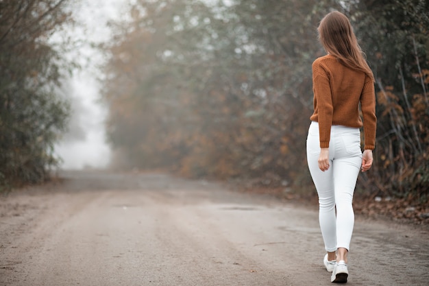 ragazza in un maglione cammina lungo una strada nebbiosa