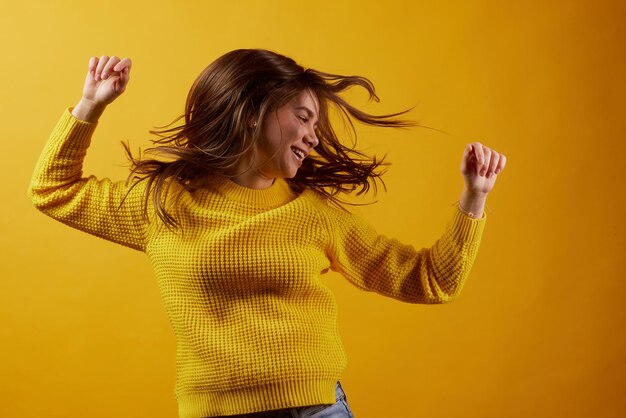 Ragazza in un maglione giallo che balla su uno sfondo giallo