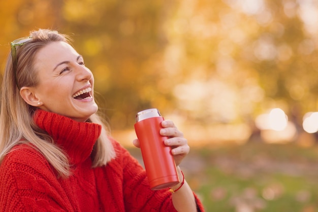 ragazza in un maglione rosso con una tazza termica in autunno nel concetto di stagione autunnale del parco