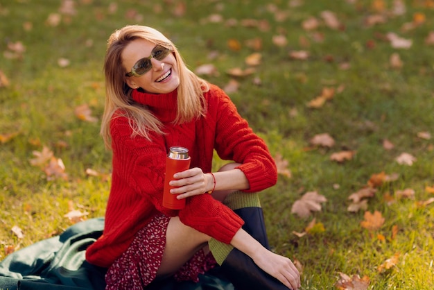 ragazza in un maglione rosso con una tazza termica in autunno nel concetto di stagione autunnale del parco