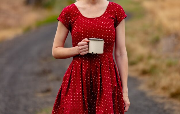 Ragazza in un vestito a pois con tazza sulla strada rurale