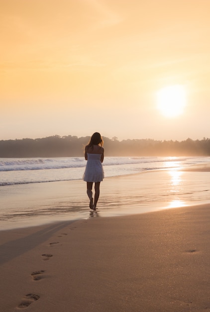 Ragazza in un vestito bianco che cammina lungo la spiaggia dell'oceano.