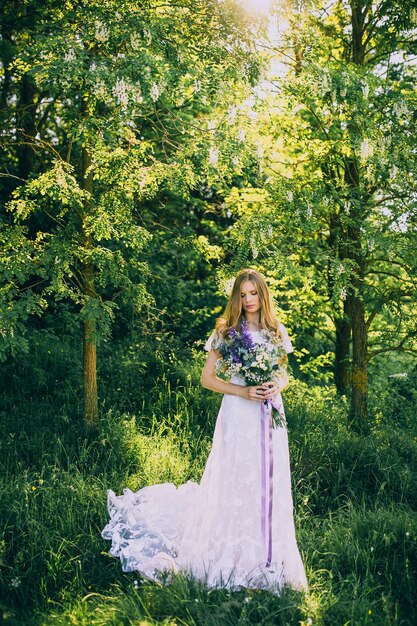 Ragazza in un vestito bianco nel prato. Donna in un bellissimo abito lungo in posa nel giardino