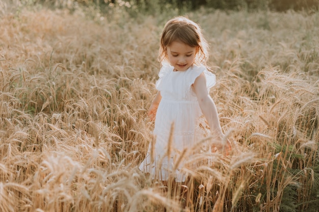 ragazza in un vestito di lino bianco in piedi su un campo di grano e toccando le spighe di grano con le mani