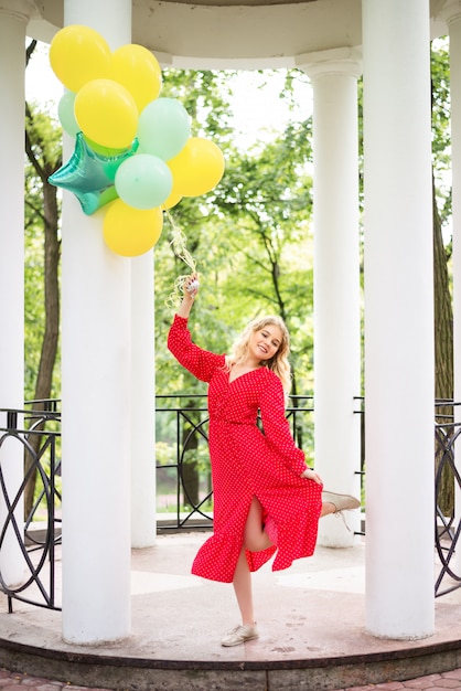 Ragazza in un vestito rosso e un mazzo di palloncini colorati nel parco