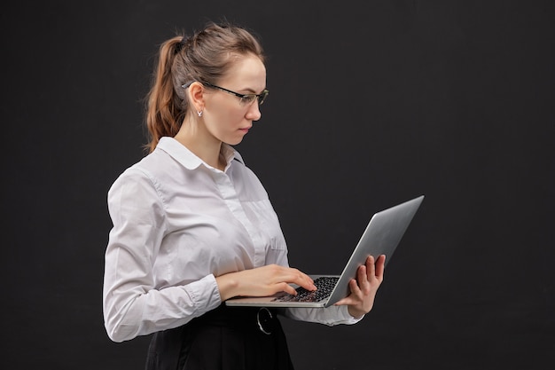 Ragazza in una camicia bianca che tiene un computer portatile su una priorità bassa nera.