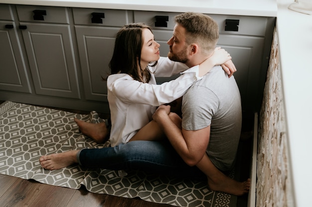 Ragazza in una camicia bianca e un ragazzo in una maglietta grigia in cucina. Baci e abbracci.