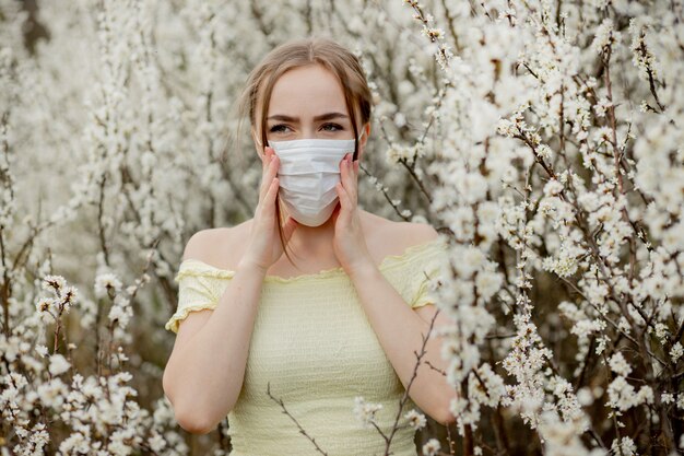 Ragazza in una mascherina medica. Ragazza in primavera tra il giardino fiorito. Una ragazza in una mascherina medica protettiva. Concetto di allergia di primavera