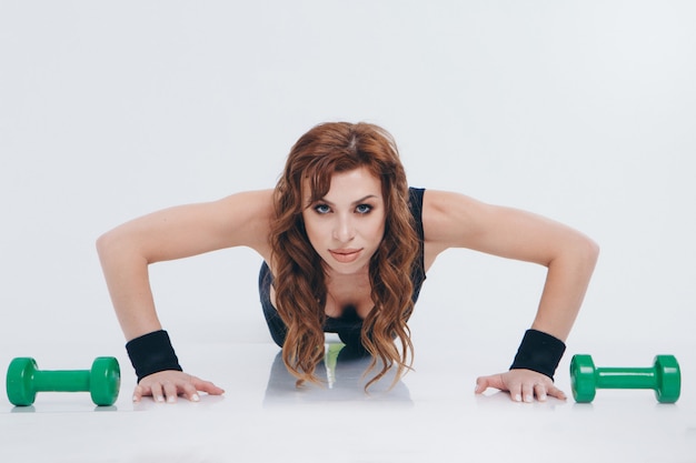 Ragazza in una tuta da ginnastica facendo esercizi con manubri, donna fa push-UPS dal pavimento. Concetto di stile di vita sano, divise sportive, coppa del mondo, palestra, abbigliamento specializzato, uniformi nere