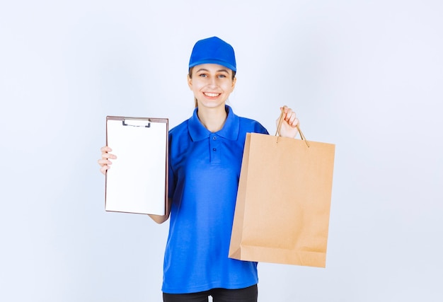 Ragazza in uniforme blu che tiene un sacchetto della spesa del cartone e un elenco di clienti.