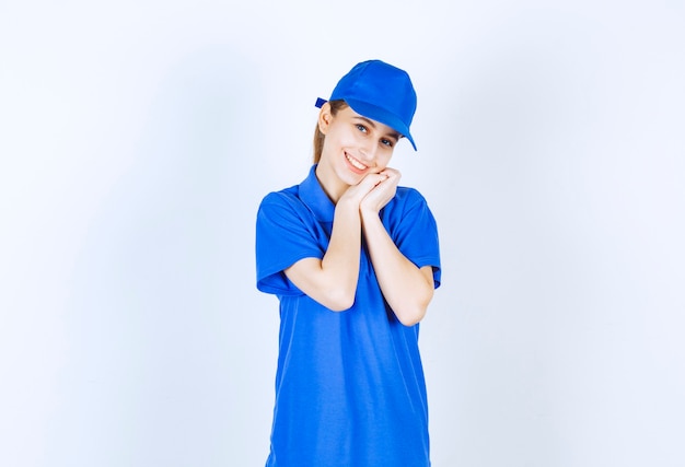 Ragazza in uniforme blu che unisce i palmi e che dà pose graziose.