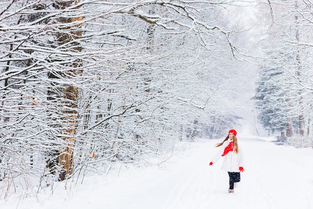 Ragazza in vestiti caldi che corre e sorride in un parco d'inverno tra la neve