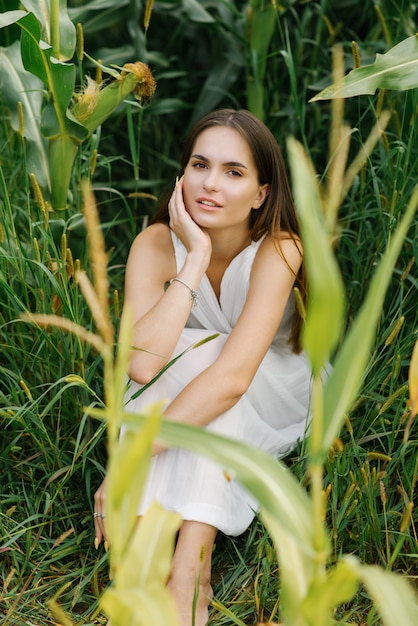 Ragazza in vestito bianco che si siede in un campo di grano verde