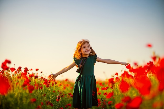 Ragazza in vestito e cappello di paglia all'aperto al campo di papaveri