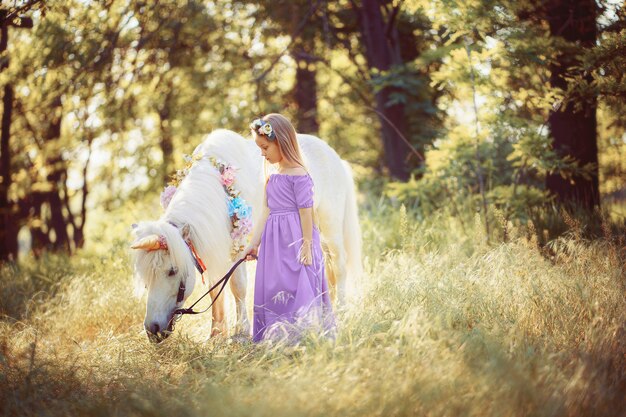 Ragazza in vestito viola che abbraccia il cavallo bianco dell'unicorno. I sogni diventano realtà. Fiaba