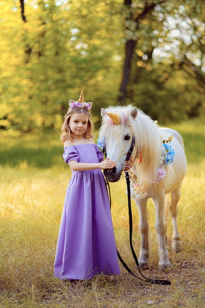 Ragazza in vestito viola con la corona di un unicorno in capelli che abbracciano cavallo bianco unicorno. I sogni diventano realtà. Fiaba