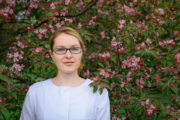 Ragazza in vetri alla moda sullo sfondo di un albero in fiore