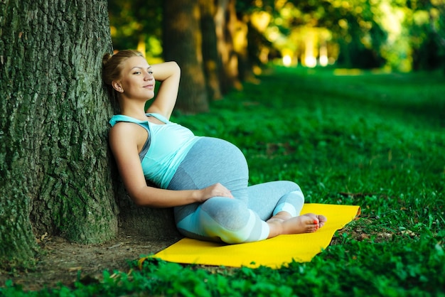 Ragazza incinta della giovane madre che riposa in un parco vicino ad un albero dopo le lezioni di yoga