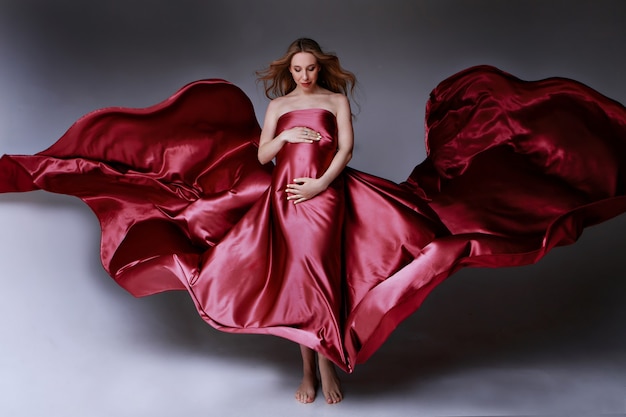 Ragazza incinta in abito rosso bellissima trama di tessuto su uno sfondo chiaro