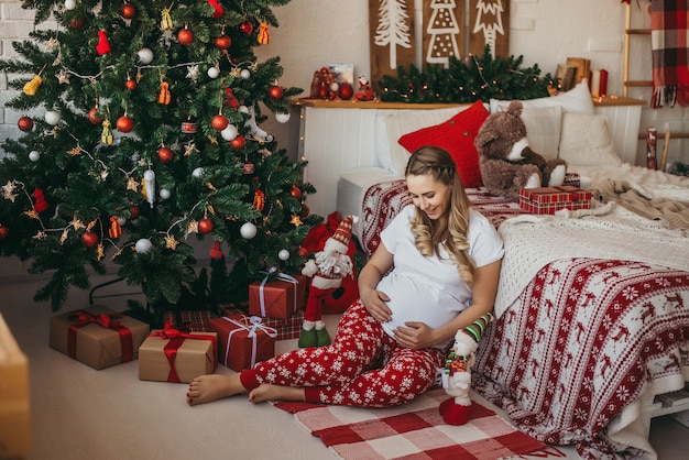 Ragazza incinta in pigiama vicino all'albero di Natale. Capodanno