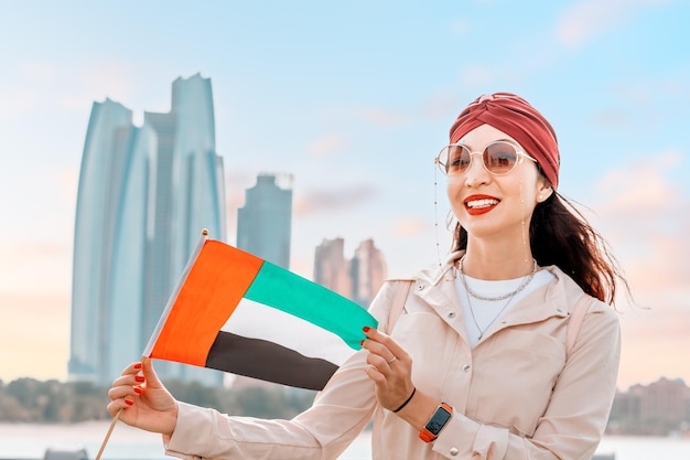 Ragazza indiana con la bandiera degli Emirati Arabi Uniti contro panoramici grattacieli ad Abu Dhabi Immigrazione istruzione studentesca e concetto di cittadinanza degli Emirati arabi