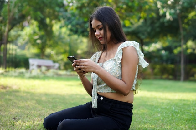 Ragazza indiana sveglia dell'adolescente che utilizza lo smartphone nel parco