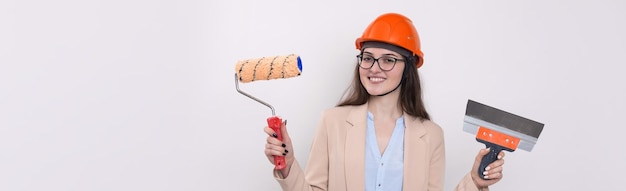 Ragazza ingegnere in un casco da costruzione arancione con intonacatura strumenti di pittura nelle sue mani su uno sfondo bianco