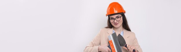 Ragazza ingegnere in un casco da costruzione arancione con intonacatura strumenti di pittura nelle sue mani su uno sfondo bianco