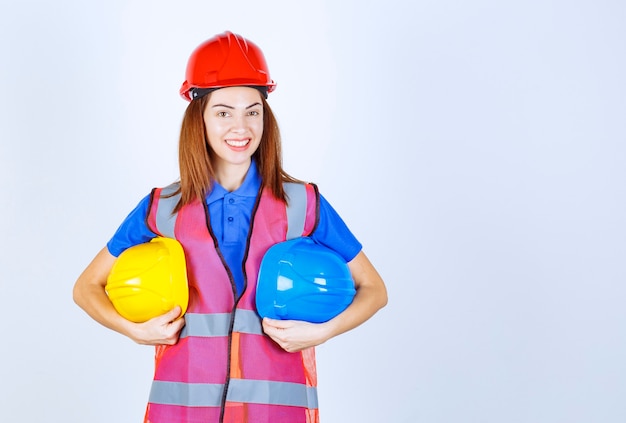 Ragazza ingegnere in uniforme che tiene caschi blu e gialli e fa una scelta.