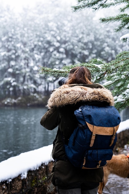 Ragazza irriconoscibile che scatta una foto al lago di una foresta di pini innevati con la fotocamera sbalordita