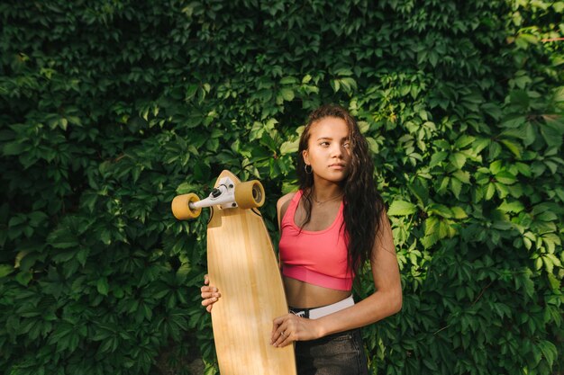 Ragazza ispanica alla moda che tiene un longboard nelle sue mani