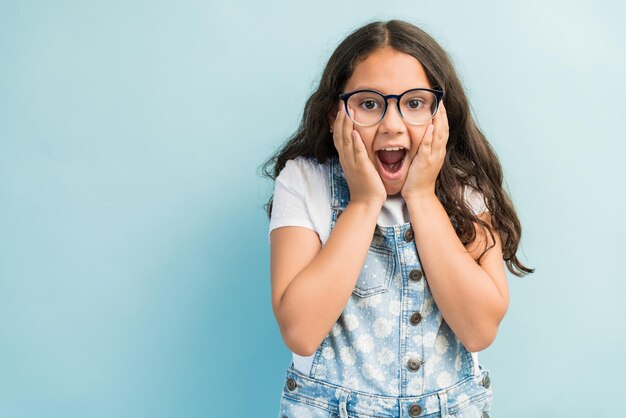 Ragazza ispanica sorpresa in piedi con le mani sulle guance che indossano tute in studio