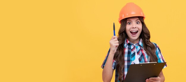 Ragazza ispirata in cappello rigido protettivo che prende appunti bambino nel progetto di lettura del casco Costruttore di bambini nel design del poster orizzontale del casco Spazio di copia dell'intestazione del banner