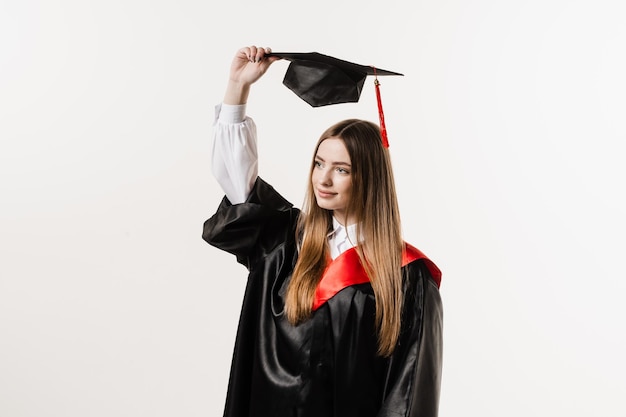 Ragazza laureata master in abito di graduazione nero indossa il cappuccio nelle mani su sfondo bianco Attraente giovane donna laureata al college