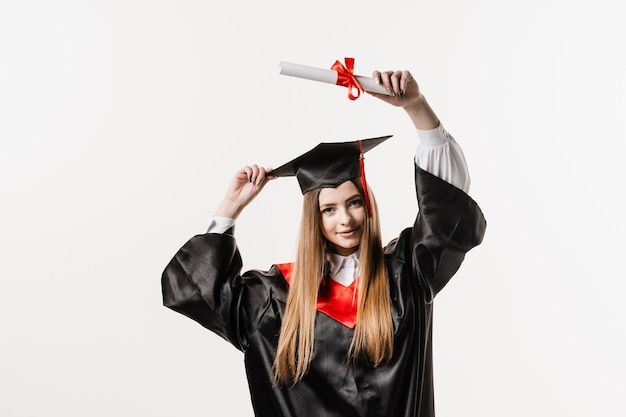 Ragazza laureata si sta laureando e festeggia il successo accademico Studentessa felice in abito da laurea nero e berretto alza il diploma di laurea magistrale sopra la testa su sfondo bianco