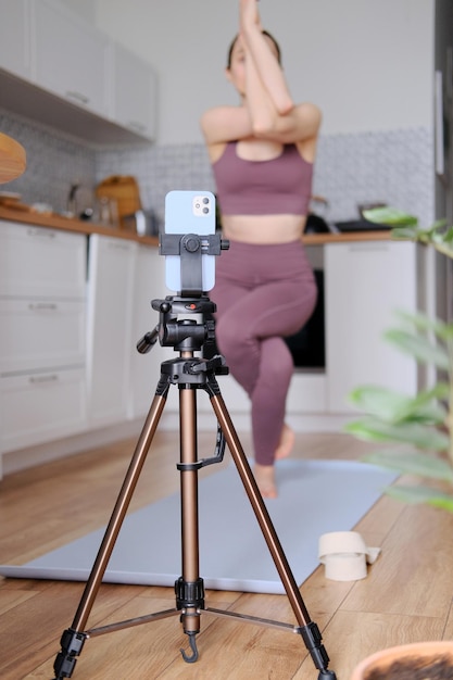 Ragazza magra che fa yoga a casa online usando il telefono e l'app