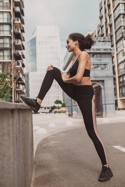Ragazza magra in abiti sportivi neri che fanno allungamento delle gambe